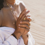Gold-toned stacked rings with colorful gemstones worn on multiple fingers of a hand.