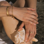 Gold ring with pale yellow citrine stone worn on hand holding seashell.