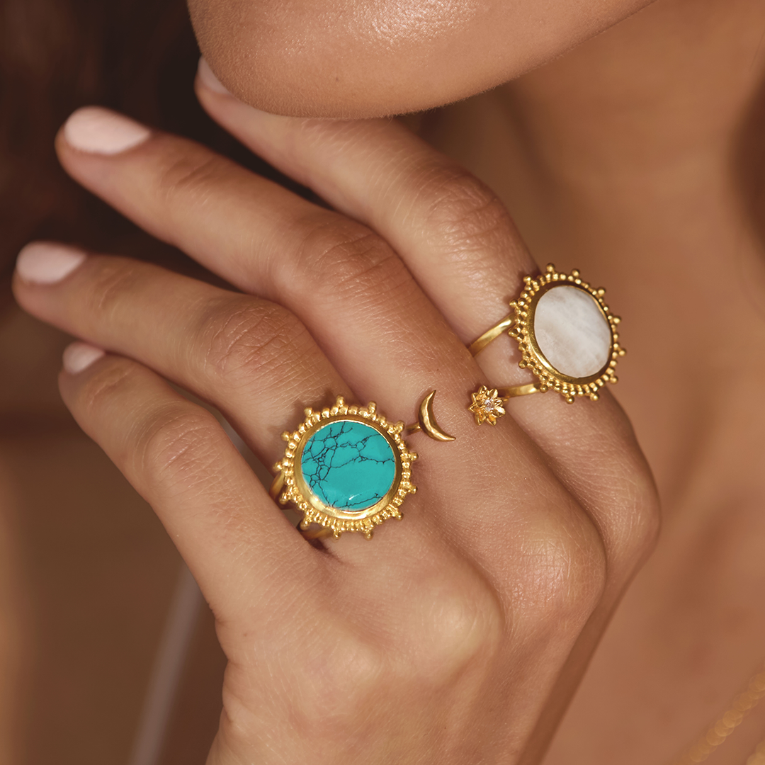 A close-up of hands adorned with various rings including the Spirit in Transformation Lotus Moon Ring, which features a small crescent moon and a lotus. This beautiful spiritual jewelry serves as a talisman for protection and is ideal for yoga practitioners and those seeking meaningful charms that enhance their meditation and zodiac connection.