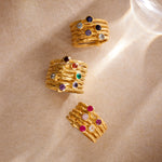 Three gold stacked rings with various colored gemstones including purple, blue, red, and clear stones set in bezel settings.