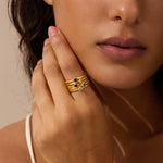 Gold stacked rings with dark and light gemstones worn on finger.