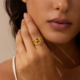 Gold stacked rings with dark and light gemstones worn on finger.