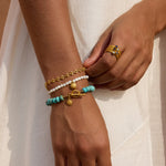 Gold stacked rings with white pearl and turquoise gemstone beads worn on hand with matching bracelets.