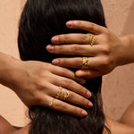 Multiple gold stacked rings with gemstones worn on fingers against black hair.