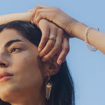 A woman showcases the Light Seeker Moonstone Starburst Nested Ring Set while holding her hair, representing spiritual jewelry that embodies clarity and protection. This piece, adorned with celestial charm, signifies meditation, manifestation, and the connection to the sun and moon, making it a meaningful talisman for yoga and zodiac enthusiasts.
