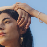 A woman showcases the Light Seeker Moonstone Starburst Nested Ring Set while holding her hair, representing spiritual jewelry that embodies clarity and protection. This piece, adorned with celestial charm, signifies meditation, manifestation, and the connection to the sun and moon, making it a meaningful talisman for yoga and zodiac enthusiasts.