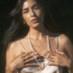 A woman in a silk top displays the Light Seeker Moonstone Starburst Nested Ring Set alongside layered necklaces, embodying the essence of spiritual jewelry and zodiac energy. This collection promotes meaningful meditation and protection, integrating the mystical themes of the sun and moon, perfect for those who value manifestation and talismans.