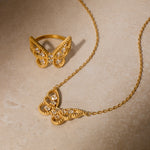 Gold butterfly ring and matching necklace pendant set with white topaz stones on textured background.