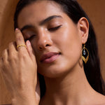 Gold textured band ring worn on ring finger of model's hand against neutral tan background.