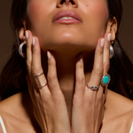 A stylish portrait of a woman adorned with multiple pieces of spiritual jewelry, including the Nurture Your Voice Turquoise Silver Ring, reflecting the essence of self-expression and meaningful charm in yoga and meditation practices.