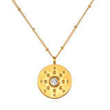 Gold-tone coin pendant with white topaz center stone and decorative studs, suspended from gold chain.