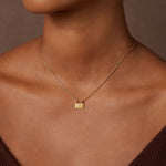 Gold-toned square pendant with white gemstone center on delicate chain worn at neck.