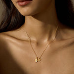 A woman wears a thin gold chain necklace with two small gold charms, a hamsa hand and an eye.