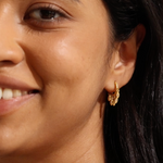 A close-up of a woman smiling, displaying the Scatter Light Huggie Earrings. These earrings embody spiritual essence and serve as a talisman for clarity and awareness, aligning with the themes of zodiac energy, meditation, and meaningful intentions in one’s spiritual journey.