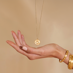 A hand gracefully holds the Joyful Beginnings Necklace, highlighting its design of a gold lotus flower and white topaz, representing protection and meaning, perfect for those seeking spiritual jewelry and meditation inspiration.