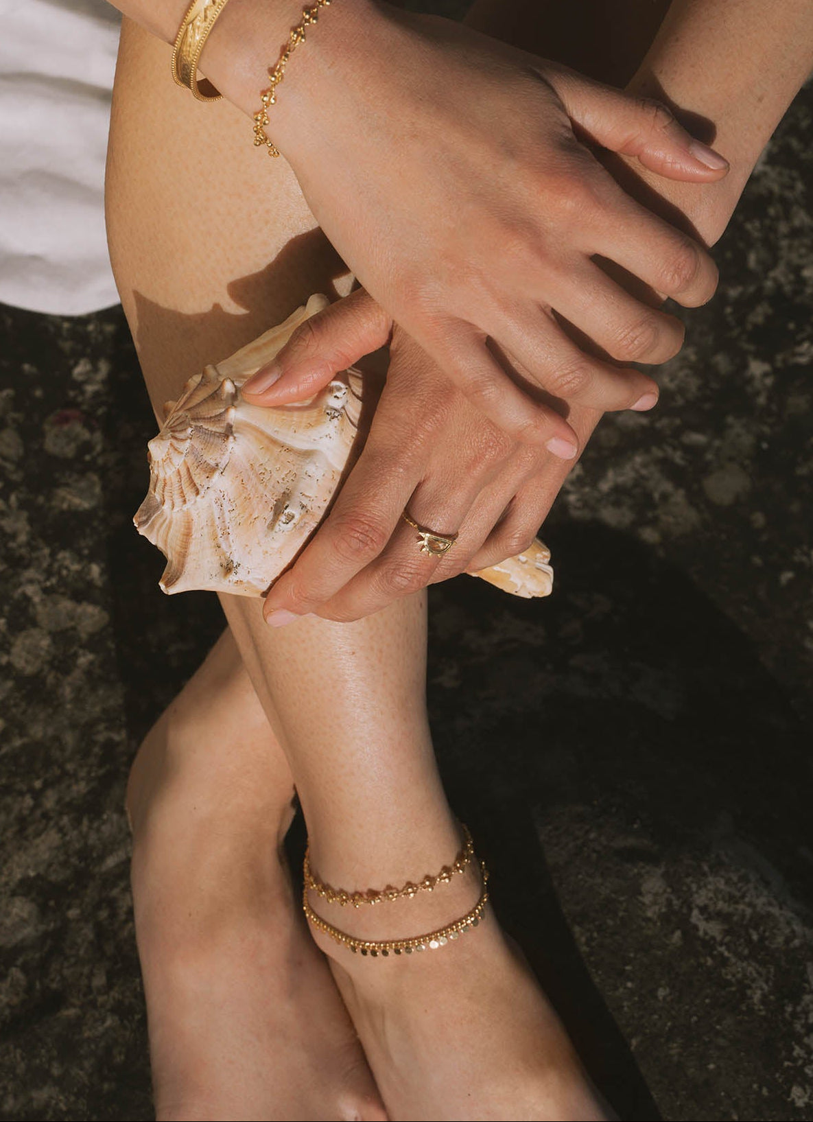 Close-up of hands and feet with gold bracelets on a dark background