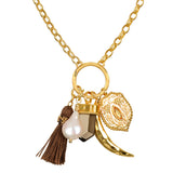 Gold chain necklace with circular pendant featuring a pearl, brown tassel, faceted stone, ornate charm, and curved gold accen