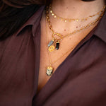 Gold layered necklaces with stone pendants worn on person in burgundy shirt.