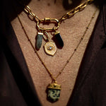 Gold chain necklace with chunky carabiner clasp holding black stone charms and a gold sunburst pendant, layered over delicate