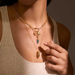 Gold-tone layered necklaces with charm pendants including a dark stone point and decorative charms worn on person.