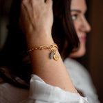 Gold chain bracelet with toggle clasp and two dangling charms: a blue-gray stone and a textured gold sunburst pendant.