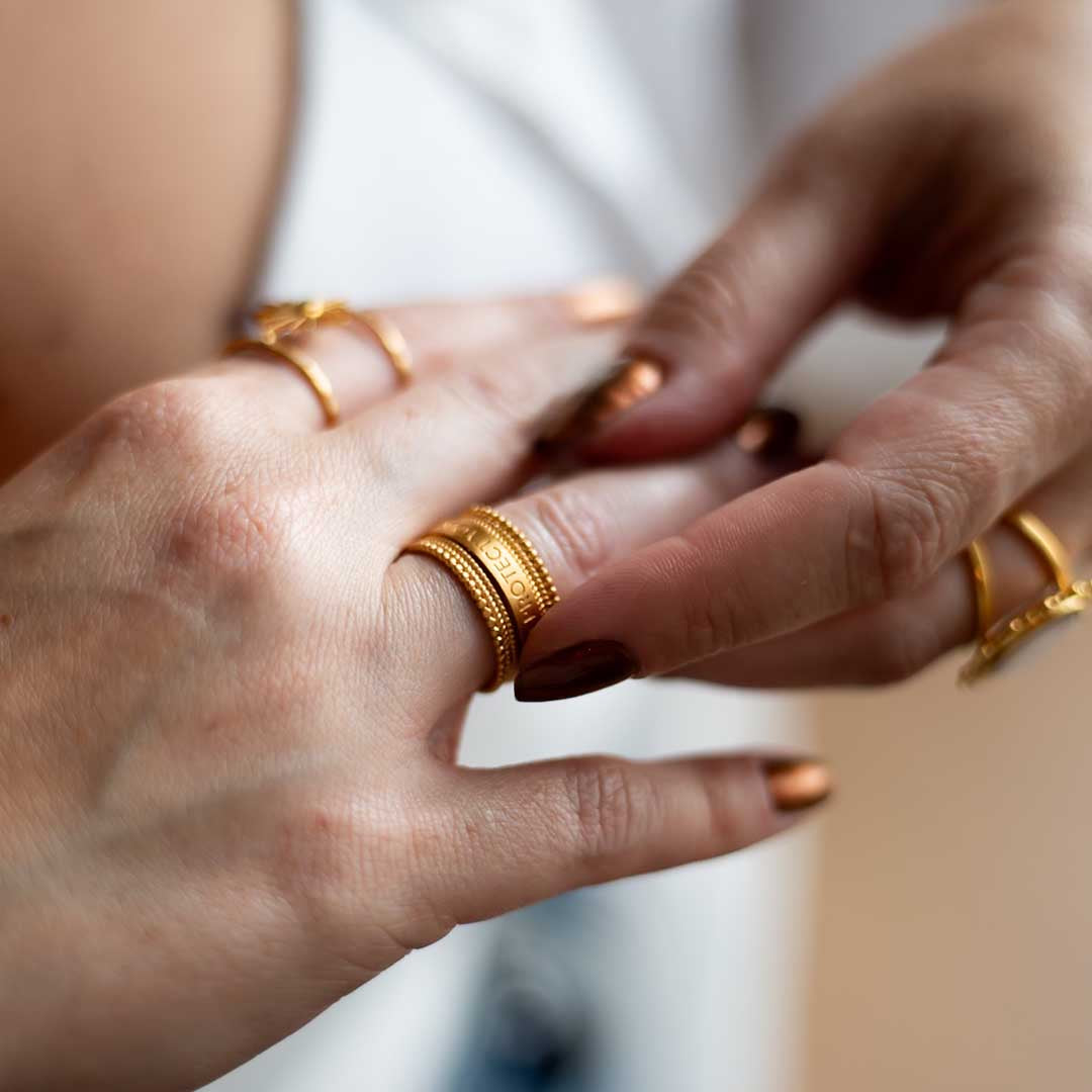 Close-up image of a hand wearing the Taryn Truly Protect Your Peace Spinner Ring surrounded by other gold rings. This shot highlights the ring's spiritual significance, making it a perfect accessory for meditation and a meaningful representation of protection and harmony.