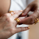 Close-up image of a hand wearing the Taryn Truly Protect Your Peace Spinner Ring surrounded by other gold rings. This shot highlights the ring's spiritual significance, making it a perfect accessory for meditation and a meaningful representation of protection and harmony.