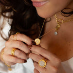 A woman delicately holding a pendant necklace alongside the Taryn Truly Protect Your Peace Spinner Ring, displaying the beauty of spiritual jewelry. This combination emphasizes the meanings behind protection and zodiac elements, ideal for meditation and self-expression.