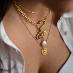 Gold layered necklaces with pearl and geometric charm pendants worn on neck.
