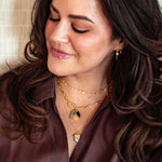 Woman wearing layered gold chain necklaces with pendant charms and matching gold earrings.