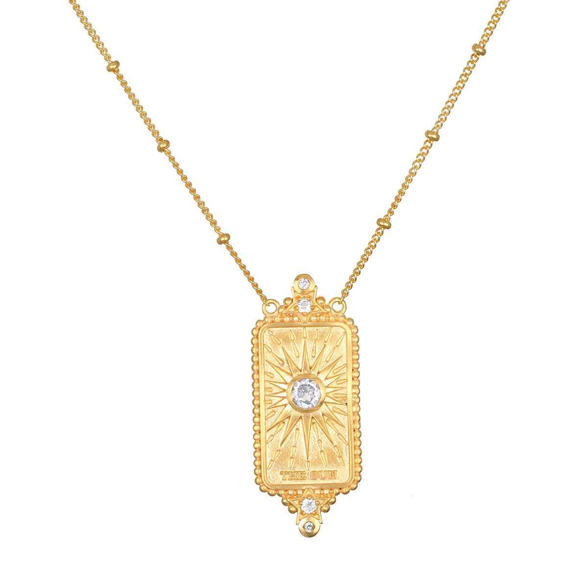 A gold pendant necklace featuring a rectangular sunburst pendant with a central clear gemstone and small accent stones, suspended from a delicate gold chain on a white background.