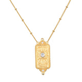 A gold pendant necklace featuring a rectangular sunburst pendant with a central clear gemstone and small accent stones, suspended from a delicate gold chain on a white background.