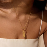 Gold-toned necklace with rectangular pendant engraved with the number 555, worn on bare chest.