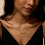A woman wearing the Capricorn Strength Zodiac Script Necklace, featuring a delicate gold chain that embodies spiritual jewelry and meditation. This meaningful talisman, perfect for zodiac enthusiasts, symbolizes resilience and manifestation, making it ideal for yoga practice.