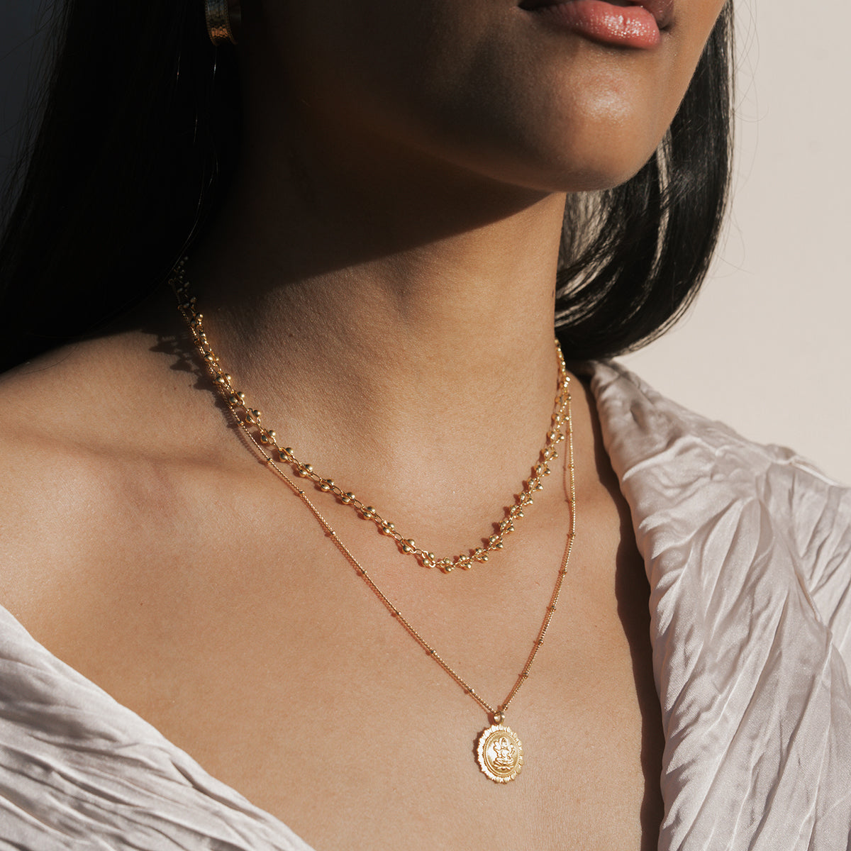 Two-layer gold necklace set with beaded chain and pendant featuring oval coin charm.