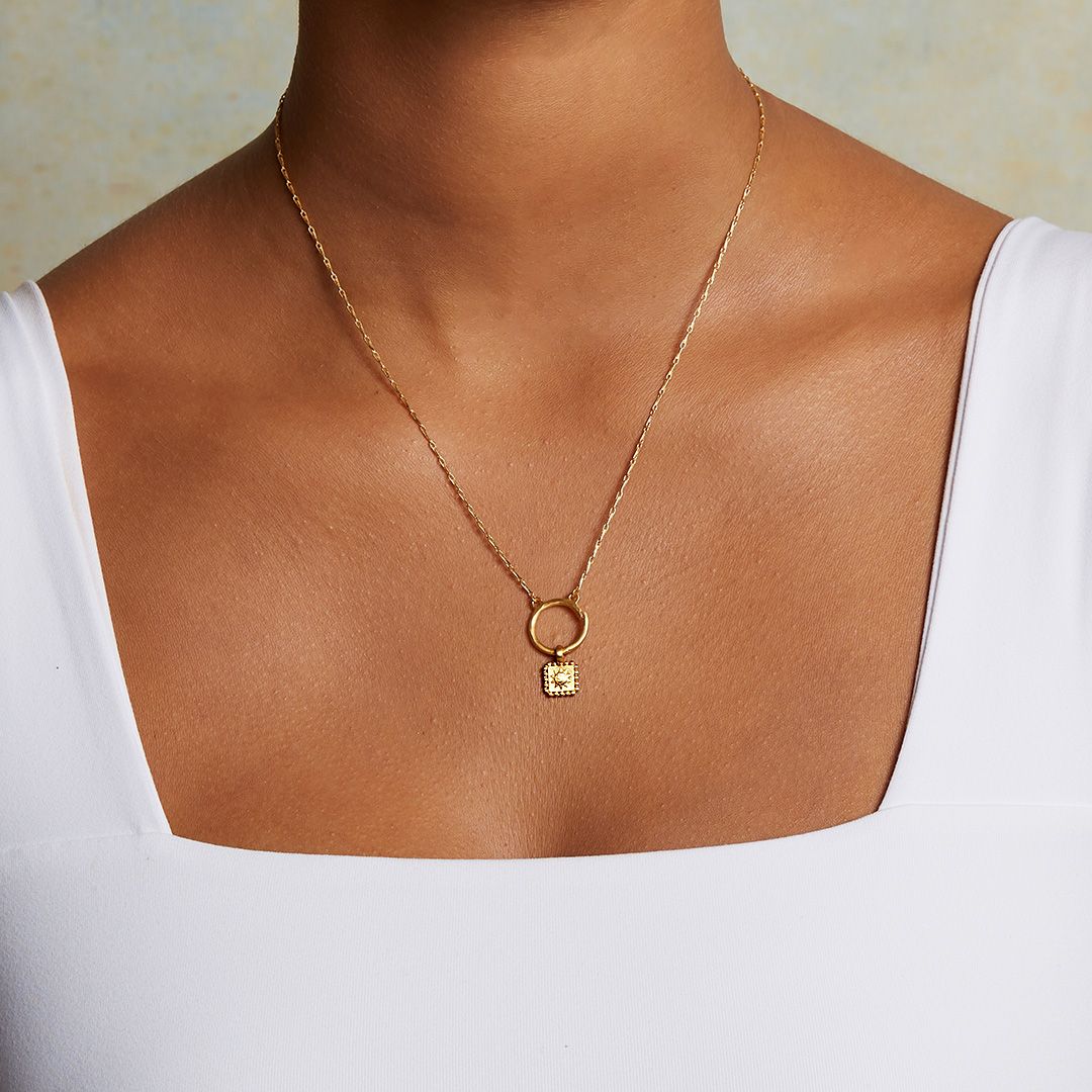Model wears the Sun Square Charm necklace, an 18kt gold plated charm symbolizing vitality and leadership, perfect for spiritual jewelry and meaningful meditation practice. This talisman complements the themes of zodiac, malas, and yoga, enhancing protection and manifestation.