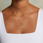 Model wears the Sun Square Charm necklace, an 18kt gold plated charm symbolizing vitality and leadership, perfect for spiritual jewelry and meaningful meditation practice. This talisman complements the themes of zodiac, malas, and yoga, enhancing protection and manifestation.