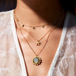 Layered view of the Pursue Your Truth Labradorite Necklace showcased against a delicate blouse. The necklace exudes elegance with its symbolic labradorite pendant, making it an ideal choice for spiritual jewelry, meditation gifts, and mantra practices. Its design not only complements yoga wear but also serves as a meaningful hamsa amulet, reflecting protection and deeper meaning in everyday wear.