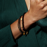 A close-up of a stylish hand showcasing multiple bracelets including the Om Black Onyx Gemstone Bracelet, ideal for mantra enthusiasts and those seeking meaningful, protective spiritual jewelry. Perfect for yoga practitioners and manifestation.