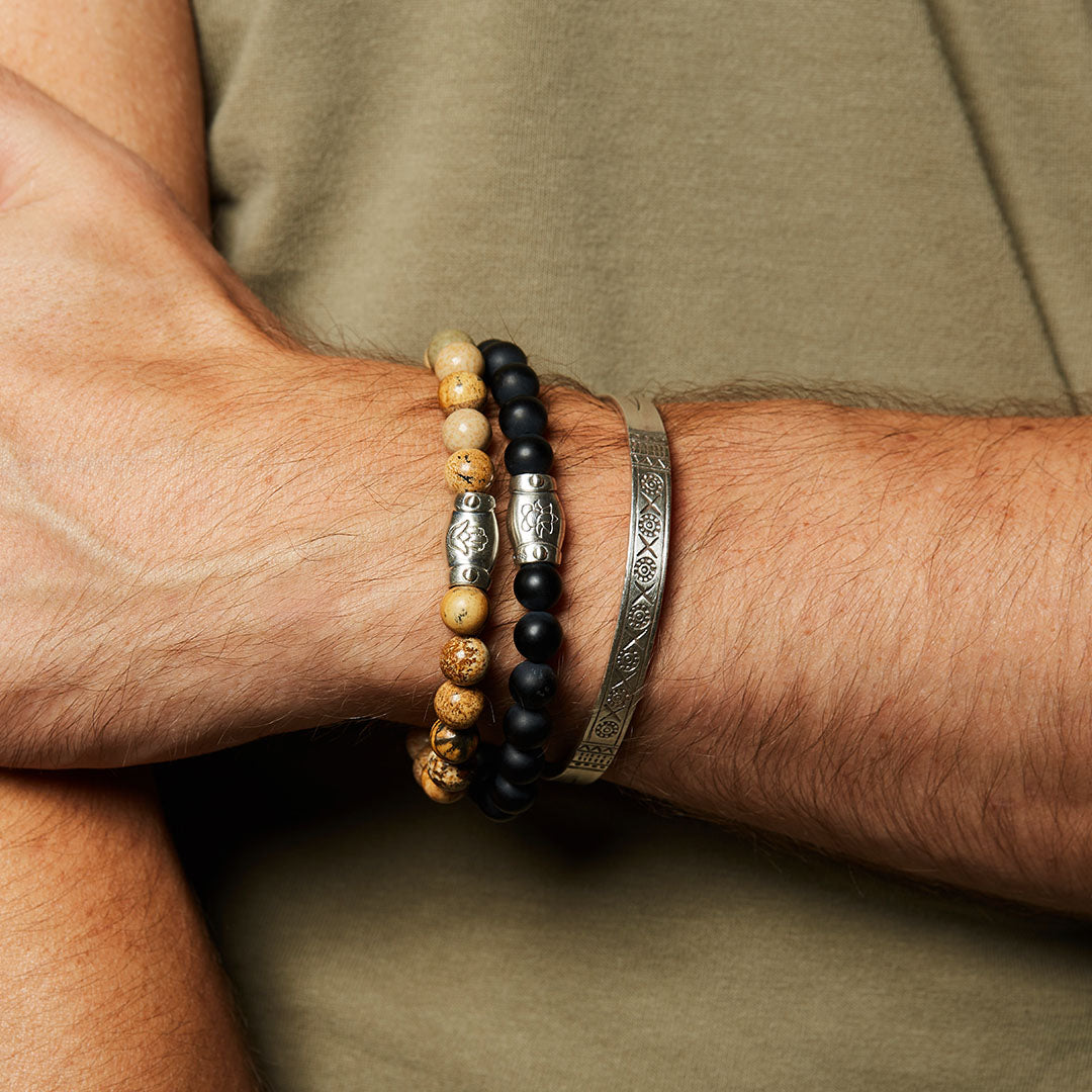 Grounded in Fortitude Sterling Silver Men's Cuff worn alongside gemstone bracelets, showcasing a layered style. This spiritual jewelry embodies the essence of meaningful protection and harmony for meditation and charm during yoga.