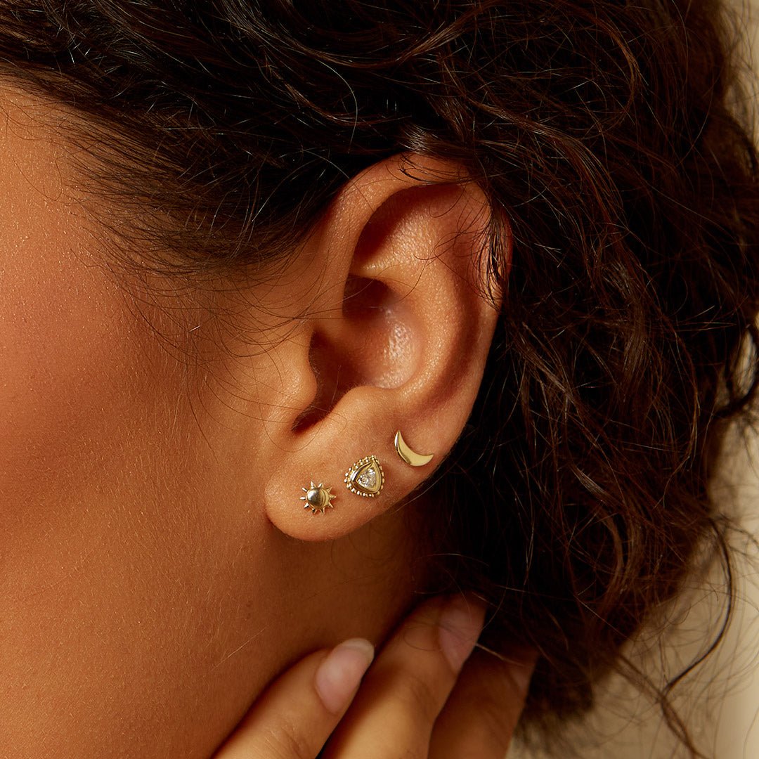 A close-up image of the Celestial Guidance 14kt Gold Sun Moon Stud Earrings worn on an ear, featuring a stylish combination of a sun and a crescent moon. These earrings are perfect for spiritual jewelry lovers seeking meaningful pieces for meditation and protection. With their charm and zodiac symbolism, they are an ideal accessory for enhancing spiritual practices like yoga and manifestation.