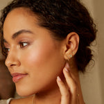 A model wearing Tiny Joys 14kt Gold Dot Huggie Mini Hoops, showcasing the delicate design of spiritual jewelry that embodies the magic of the Universe, perfect for meditation, talisman, and meaningful moments in life.