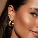Model smiling while wearing the Light and Love Gold Ear Cuff in an elegant ear stack, featuring other gold accessories. This ear cuff represents the essence of spiritual jewelry, merging protection and manifestation in a stylish way, perfect for zodiac enthusiasts and yoga practitioners.