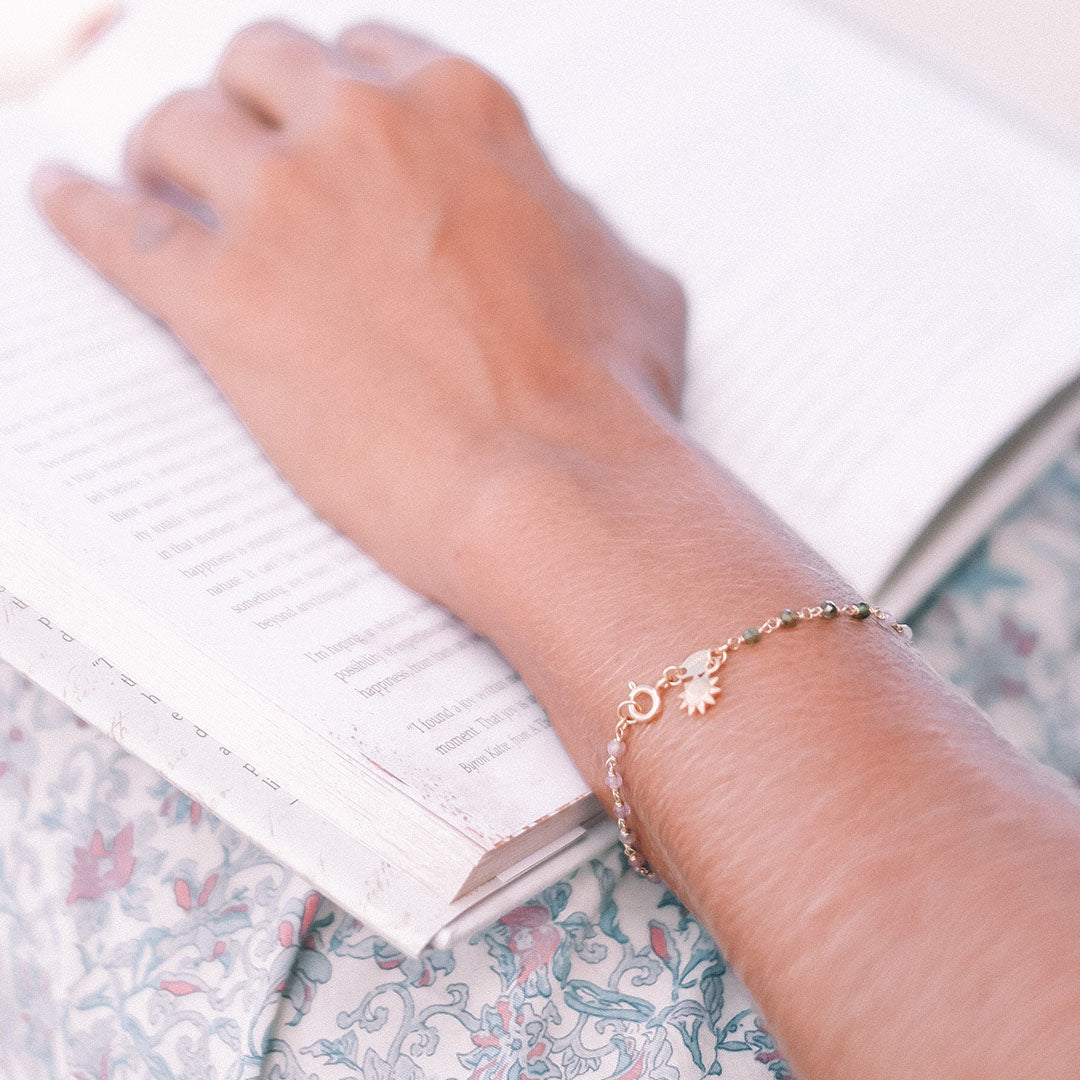 A close-up of a person wearing the Abundant Joy Tourmaline Gemstone Bracelet while reading a book. The bracelet, featuring tourmaline stones and a sun pendant, symbolizes vitality and leadership, making it a perfect piece of spiritual jewelry for meditation and manifestation.
