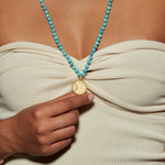 A model wearing the Beyond the Horizon Turquoise Mala, showcasing the golden medallion and turquoise beads, symbolizing yoga and spirituality. This meaningful necklace is ideal for harnessing energy and serves as a charm for self-expression and protection during meditation.