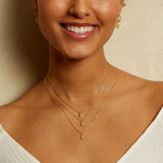 Multiple layers of necklaces, including the Lucent Spirit Mini Sun Pendant Necklace, worn by a smiling model. This beautiful collection signifies the importance of spiritual jewelry and charms in personal style, enhancing your meditation and yoga sessions with protection and meaning.