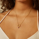 A model wearing a Pink Tourmaline Bezel Charm on a delicate gold necklace, highlighting the charm's vibrant color and design. This piece of spiritual jewelry is significant for those who practice yoga and seek meaningful adornments that represent the sun, moon, and zodiac.