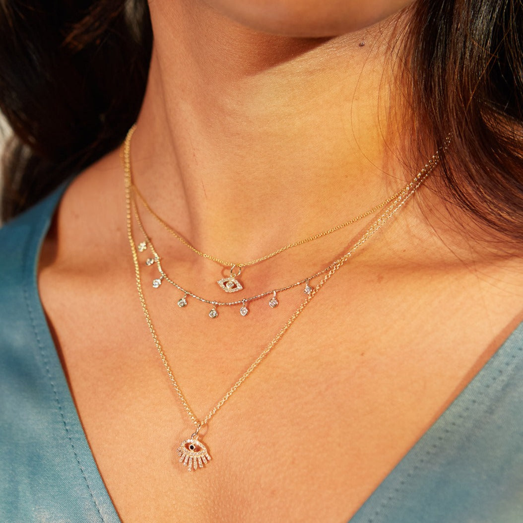 Gold layered necklaces with diamond and eye-shaped pendants worn on person.
