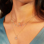 Gold layered necklaces with diamond and eye-shaped pendants worn on person.