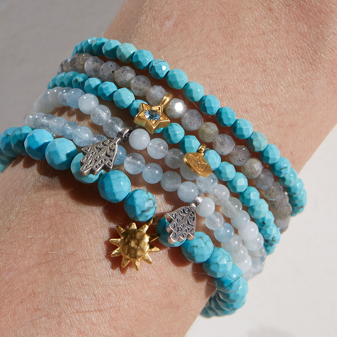 A stack of gemstone bracelets including the Inner Voice Lotus Gemstone Bracelet, showcasing vibrant turquoise and various charms. Ideal for yoga and spiritual practice, these malas serve as talismans for protection and meaningful self-expression.
